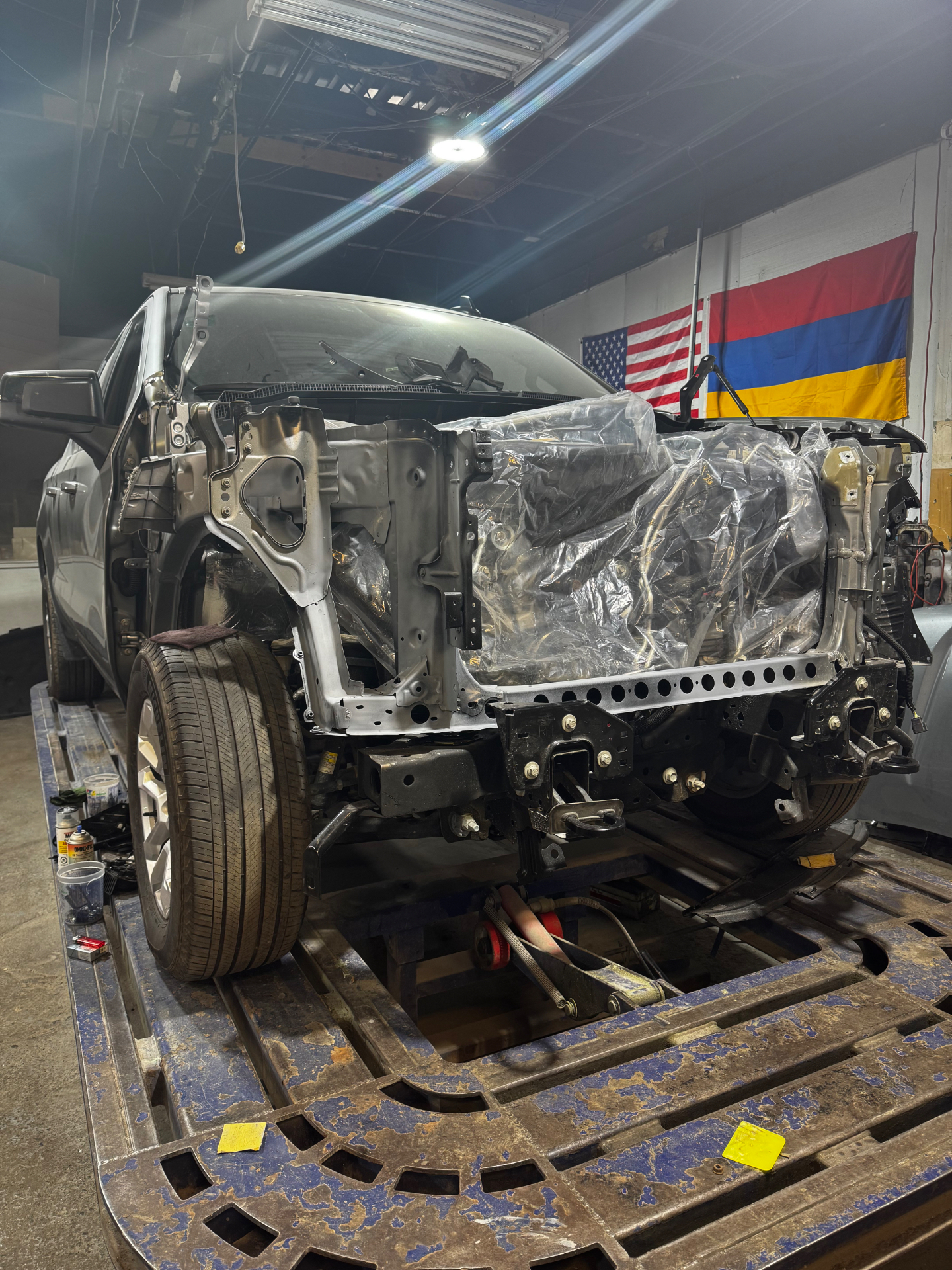 Silver SUV with the front end disassembled on the frame bench in the shop