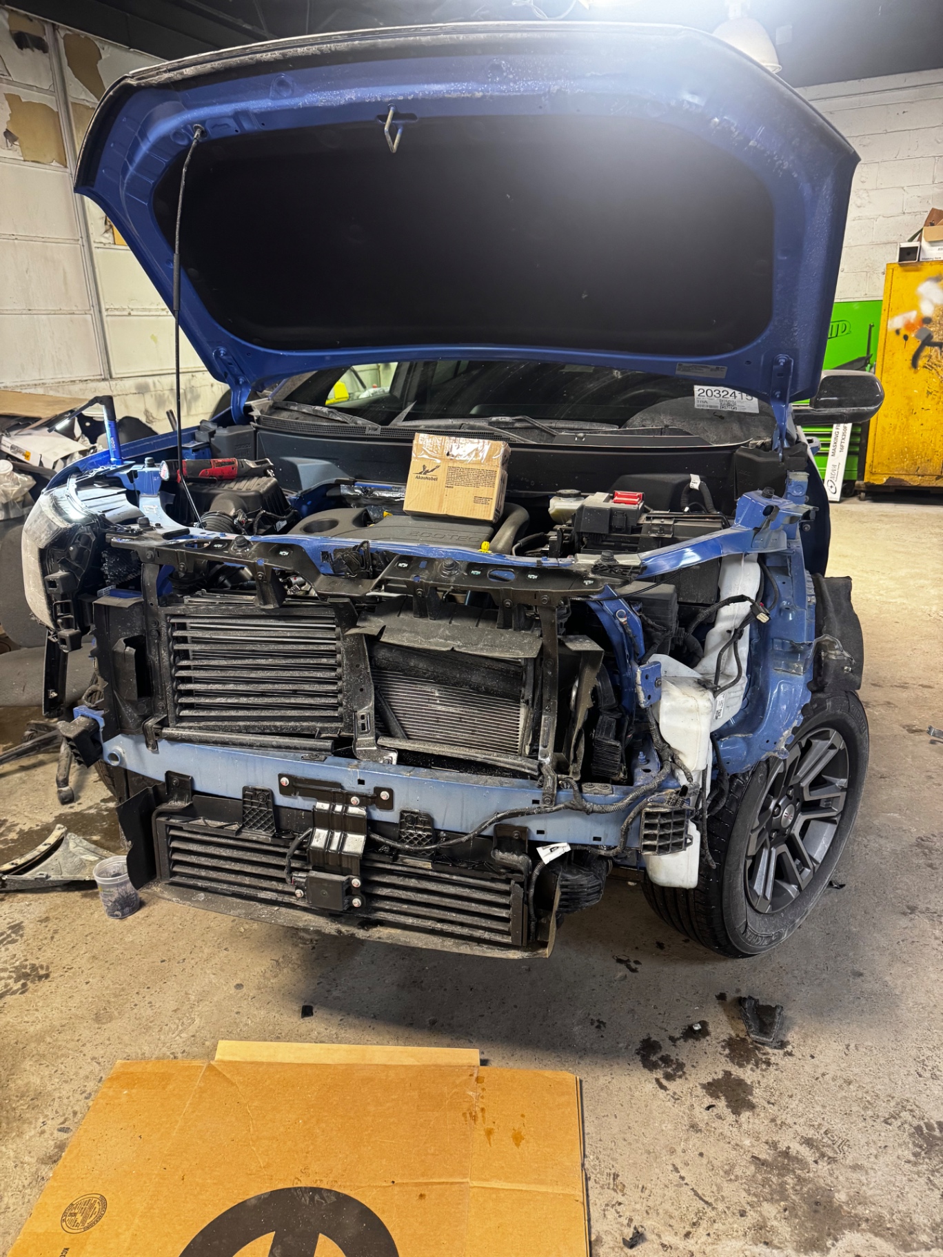 Blue Ford with the hood open and the front end disassembled, before repair